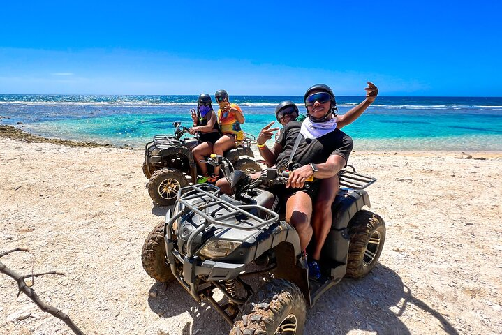 Group riding ATVs by Roatan sign